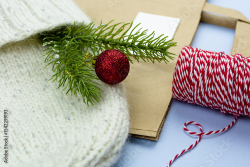 A spruce branch with a Christmas tree toy in a winter hat, two-color thread and a craft bag on a blue table. New Year's composition.