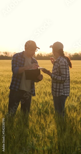 vertical Two farmers in wheat field at sunset discussing investment planning. Farmers working on investment strategies for crop growth and development. Discussion of investment in agriculture.