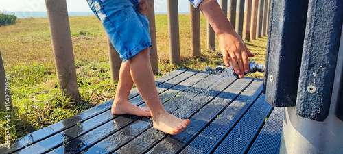 Boy, toddler washes his feet from sand under the shower on the beach of Portugal close-up. Concept of summer, beach vacation with a child