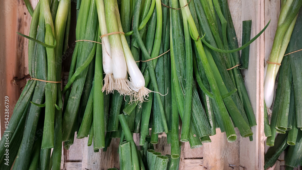 Obraz premium Fresh green onions tied together, showcasing vibrant colors and textures in a rustic setting