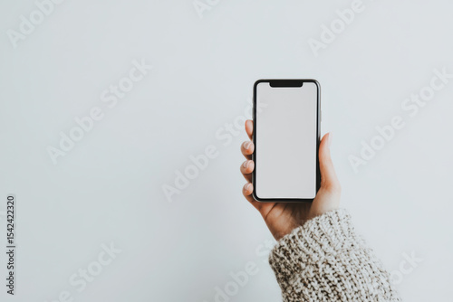 Cozy close-up of hand holding smartphone in soft natural light with knit sweater and calm atmosphere, mockup