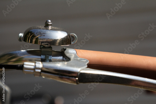 A classic metal bike bell mounted on the handlebar, symbolizing vintage charm and functional design. The reflective surface catches the light for an eye-catching detail.