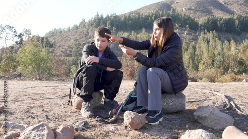 Young hikers are resting on some rocks during a hike in the mountain and are using a smartphone