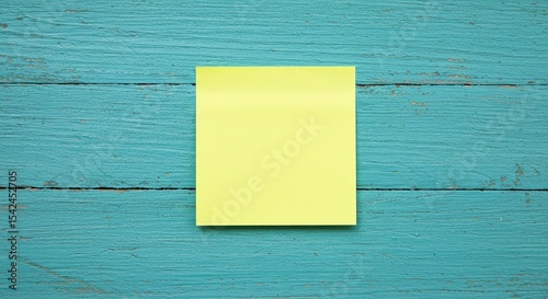 A yellow, square-shaped adhesive note is placed on a blue wooden background, creating a simple yet striking visual contrast.