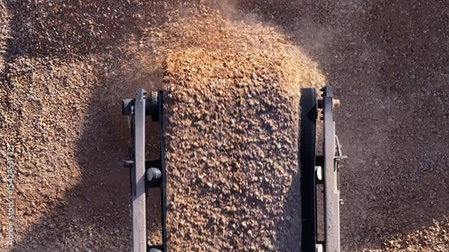 Close-up, top-down aerial of a conveyor belt dropping a continuous stream of crushed stone onto a large stockpile. Seamless loop of industrial aggregate production.
