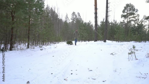 Man dragging a freshly cut christmas tree through a snowy forest path