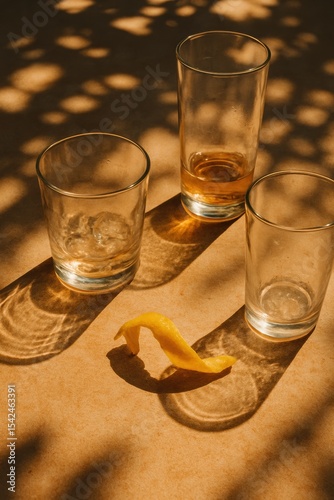 Empty glasses and lemon peel on sunlit table with artistic shadow play