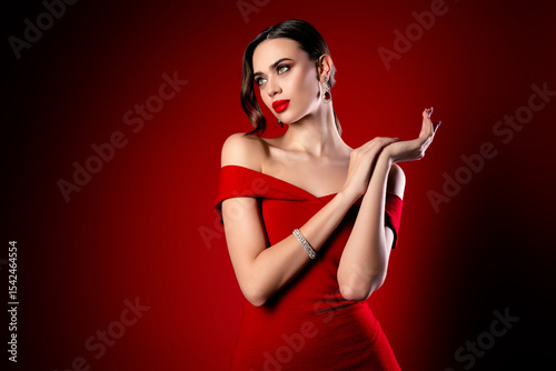 Elegant brunette woman in red dress posing stylishly with jewelry for fashion and luxury concepts