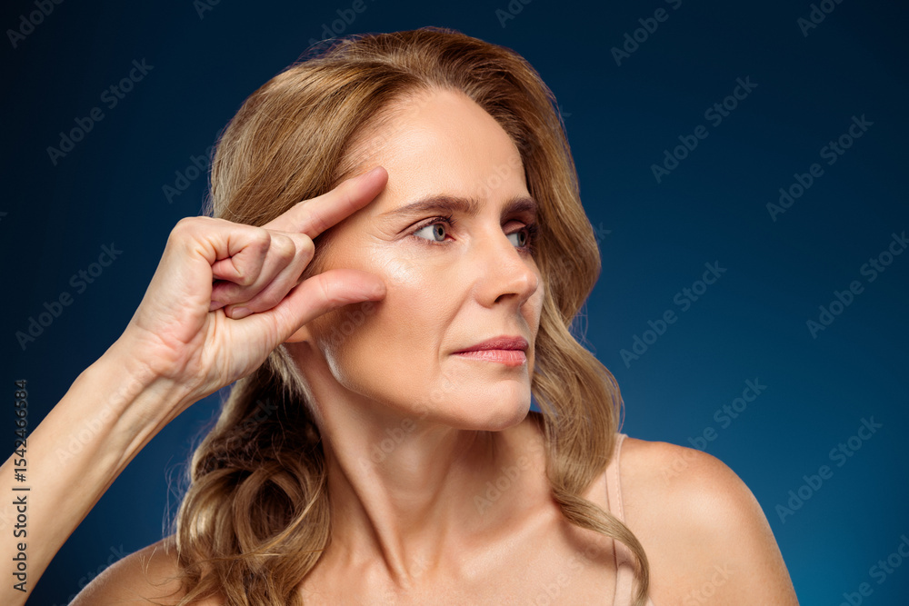 Fototapeta premium Elegant middle aged female posing against blue background with gentle expression and confident demeanor