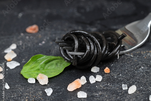 black pasta with cuttlefish ink and green basil leaves on a black fork. Pasta of durum wheat semolina with squid ink.