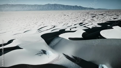 Monochromatic aerial view captures vast desert landscape with undulating sand dunes casting deep shadows, creating a serene and dramatic visual narrative.