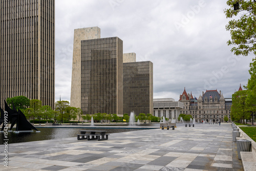 Historic architecture and modern buildings blend in Albany, New York, showcasing urban landscape and serene water features under cloudy skies
