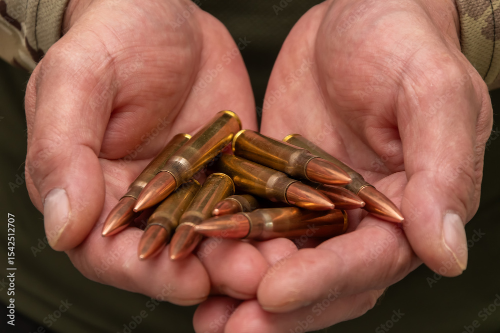 Fototapeta premium Male hands in military garb hold several large cartridges. The close-up symbolises the theme of war, weaponry, threat and self-defence.
