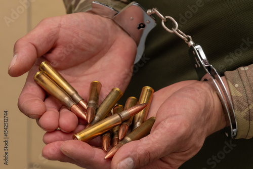 Handcuffed hands of a man in camouflage holding ammunition. The scene symbolises war crimes, illegal possession of ammunition.
