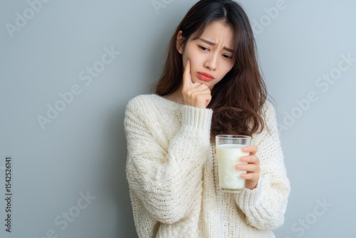 Young Asian woman hesitates with a glass of milk concerned about stomach upset due to lactose intolerance