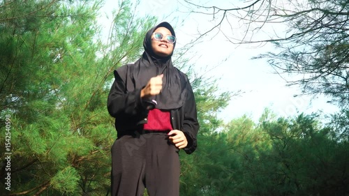 Muslim woman wearing hijab doing workout in the morning. Background of pine tree leaves