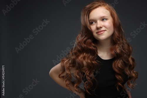 Portrait of beautiful teenage girl with healthy wavy hair on dark grey background. Space for text