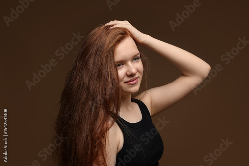 Beautiful teenage girl with healthy wavy hair on brown background