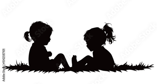 Two young children playing together on the grass in silhouette.