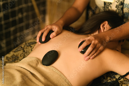 Professional therapist performing soothing hot stone massage treatment on woman's back in elegant hotel spa