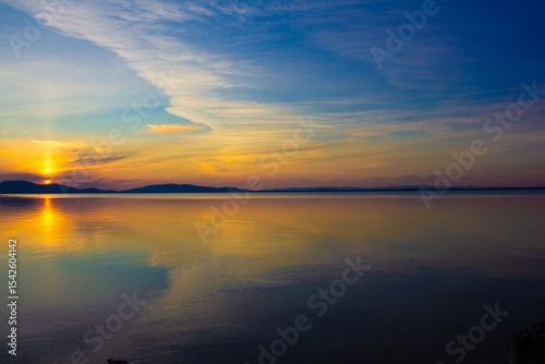  Stunning sunset over calm lake with vibrant colorful sky, dramatic clouds, and perfect reflection in water. Serene nature landscape ideal for backgrounds, banners, travel, meditation, and relaxation.