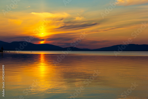Golden sunset over tranquil lake with colorful sky and smooth reflections. Serene evening scene with mountain silhouettes, glowing horizon and peaceful nature. Perfect for travel and landscape themes.