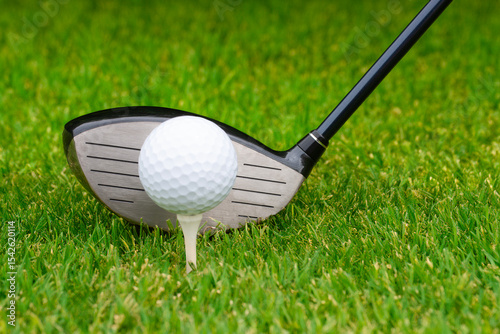Close up of golf ball on tee with driver behind it.