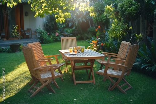 Wooden outdoor table with four matching chairs on green grass in sunlit garden surrounded by lush tropical plants and flowers