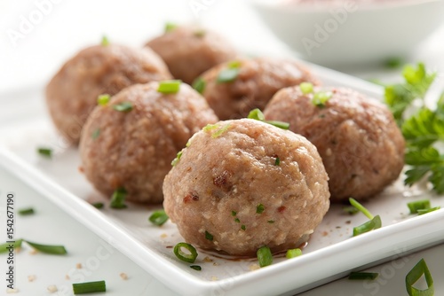 A plate of cooked meatballs garnished with herbs on a white background.