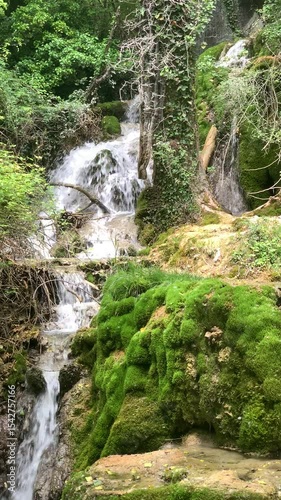 A waterfall with moss growing on the rocks. The water is clear and the moss is green. The scene is peaceful and serene