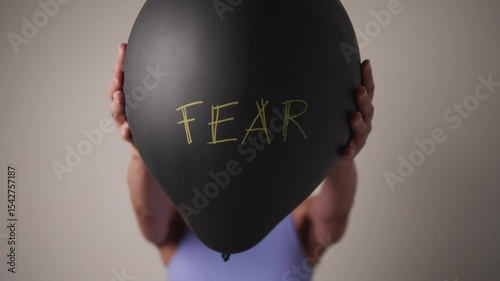 A person offering a balloon labeled FEAR directly toward the camera, representing confrontation with emotion.