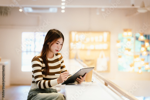 A young woman wearing headphones and glasses, appearing to be an East Asian female, intently uses a white laptop at a cafe table. photo