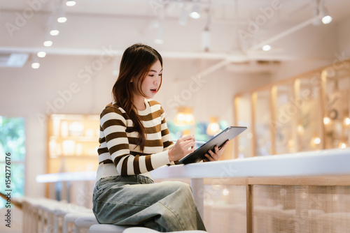 A young woman wearing headphones and glasses, appearing to be an East Asian female, intently uses a white laptop at a cafe table. photo