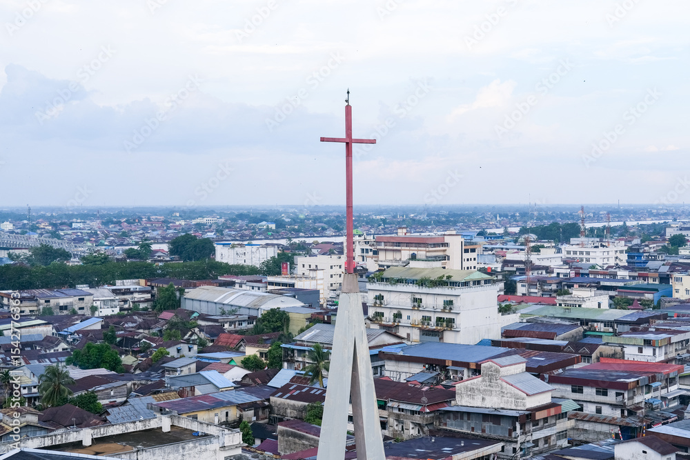 Obraz premium Skyline of Pontianak city reflecting its ethnic and religious diversity, marked by a church steeple standing tall among dense urban housing and commercial buildings.