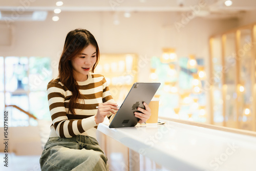 A young woman wearing headphones and glasses, appearing to be an East Asian female, intently uses a white laptop at a cafe table. photo
