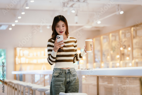 A young woman wearing headphones and glasses, appearing to be an East Asian female, intently uses a white laptop at a cafe table.