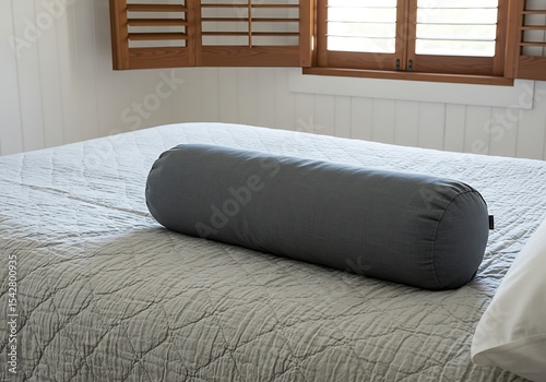 Cozy bedroom scene featuring a bolster pillow on a quilted bedspread, minimal decor