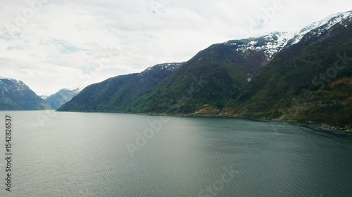 Majestic Hardanger fjord with deep tranquil waters stretches to horizon among mountains covered with snow. Higher peaks under overcast sky in Norway