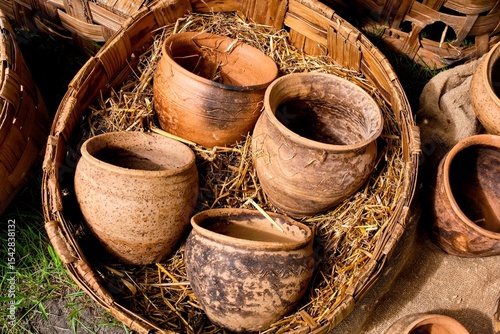 Ancient Style Clay Vessels in Wicker Basket. Old-fashioned Ceramic Containers in Outdoor Market Setting.