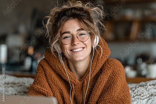 Portrait of a smiling woman wearing glasses and headphones, talking on a laptop.