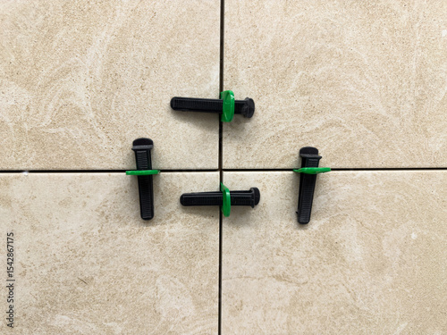 Close up of beige ceramic tiles aligned with tile leveling system. Precision tools create straight grout lines and a smooth, professional finish during modern interior installation work
