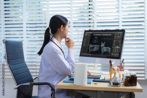 A confident Asian female veterinarian sits at her desk, providing online consultations. She uses computer and monitor to diagnose and advise pet owners, offering virtual care through  animal clinic.