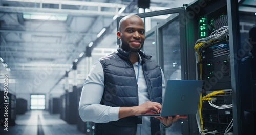 Wallpaper Mural Portrait of a Data Center Engineer Using a Laptop Computer. Young Black Man Looking at Camera and Smiling. Information Technology Specialist Standing in a Server Room Facility at a Research Center Torontodigital.ca