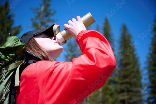 Woman in hiking gear taking a sip of water during mountain hike. Sporty female standing in front of snowy peaks.