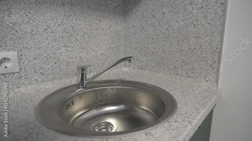 Stainless sink built into countertop rests near socket. Compact arrangement ideal for quick tasks. Accessible plug adds versatile utility