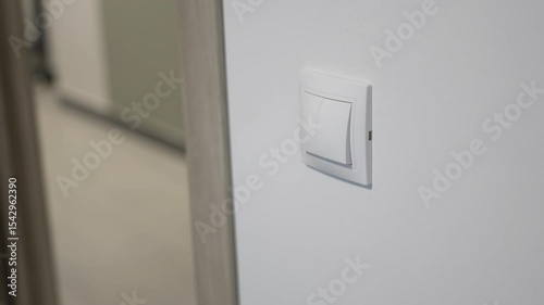 Bright white light switch mounted cleanly beside rough doorway. Smooth plastic contrasts textured wall surface for minimalist look