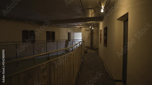 Plastic-covered handrails trace perimeter of rough concrete surfaces. Temporary bulbs project sharp shadows over plain, unfinished surfaces
