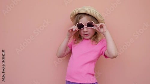 Young girl poses stylishly with sunglasses against a pastel wall backdrop