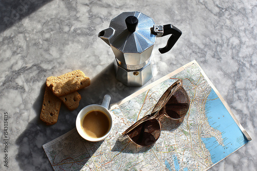 Flat lay of a travel scene with a moka pot, espresso cup, cookies, sunglasses, and a city map arranged on a marble surface