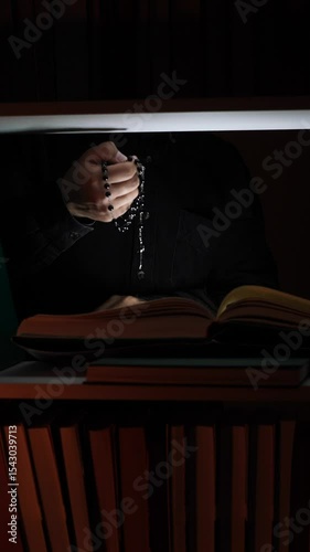 vertical video Priest praying with rosary and reading holy bible in dark library